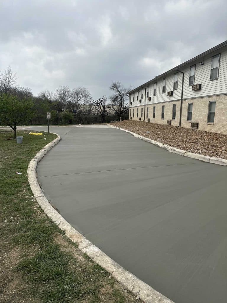 Wide concrete drive freshly poured next to a multifamily apartment complex